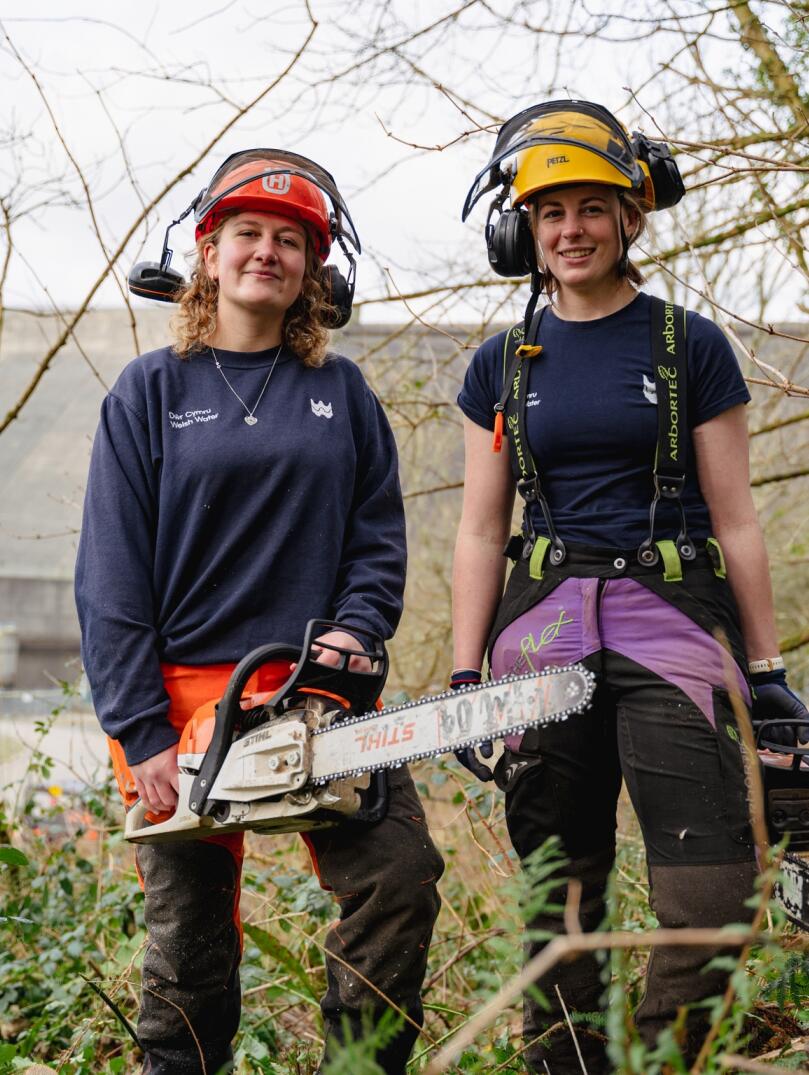 Llys y Fran Rangers wear protective equipment and hold chainsaws in the forest (left to right- Katie and Millie)