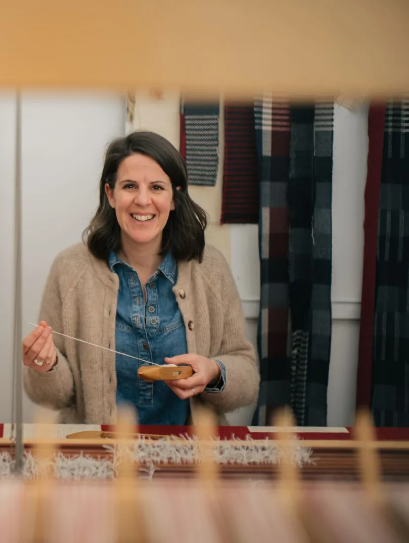 Welsh textile artist Llio James sitting at her hand weaving loom, smiling at the camera