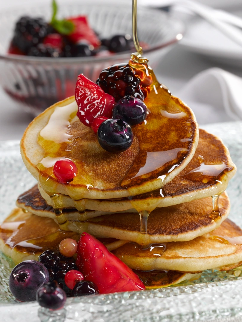 A pile of crempog (Welsh pancakes) with berries and syrup