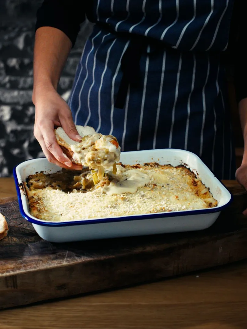 A roasting tin with freshly baked Anglesey eggs, with a chef's hand scooping some out on a slice of cut bread