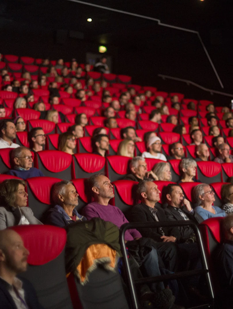 Audience seated in red chairs inside a cinema auditorium