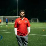 Club founder Delwyn Derrick standing on a football pitch while a game takes places behind him