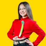 Young girl in a Welsh hat and red jumper standing showing off a leek pinned to her jumper