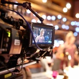 A professional camera in a studio where filming is taking place, with an actor showing through the viewfinder