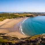 A wide sandy cove with blue seas and cliffs.