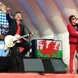 Two people playing guitars and singing on a stage.