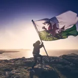 A person on a windy mountain holding a large Welsh flag