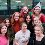 9 young women crouched in front of Urdd logo