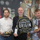 Three men holding their products smiling at the camera.