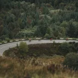 Four cyclists in red jerseys cycling round a tight bend in a mountainous road, surrounded by a mixture of beautiful trees