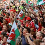 A crowd of football supporters holding Welsh flags.