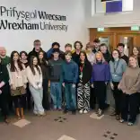 A group of young people and adults standing together inside a university building. They are posing for a group photo in a bright indoor space. 