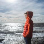 A man in an warm orange jacket looking out to sea