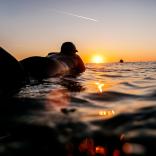 日が沈む中、サーフボードに横たわって波に乗るのを待っている人