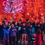 A male voice choir singing in front of a castle that is lit up in red 