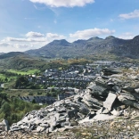 Ein Berg mit Schieferabraum im Vordergrund und Bergarbeiterhäusern und Bergen dahinter