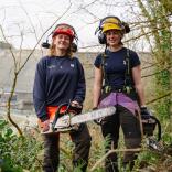 Llys y Fran Rangers wear protective equipment and hold chainsaws in the forest (left to right- Katie and Millie)