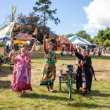 Tres personas vestidas con trajes de festival brillantes levantando los brazos para saludar