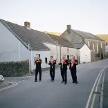 Cuatro miembros de una banda de metales tradicional galesa tocando sus instrumentos, caminando por una calle típica de los valles galeses.