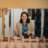 La artista textil galesa Llío James sentada en su telar manual, sonriendo a la cámara.