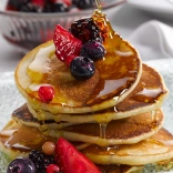 A pile of crempog (Welsh pancakes) with berries and syrup