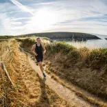 A person running over the cliffs in Pembrokeshire with the sea in the background.