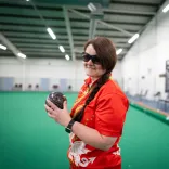 Julie Thomas holding a bowls ball on an indoor bowling green for Team Wales.